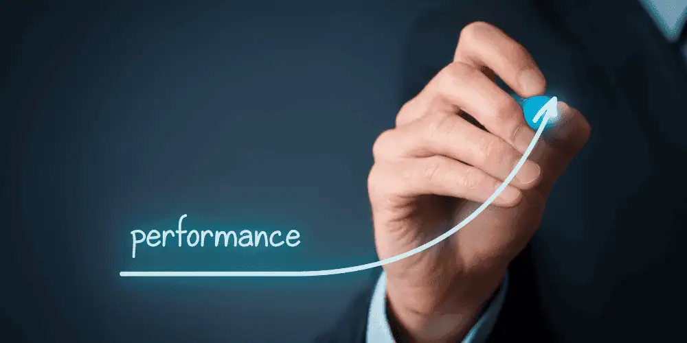 A person in a suit draws an upward-curving line with the word performance, symbolizing efforts to improve performance and growth, on a transparent screen against a dark background.
